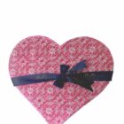 Tapa decorativa de una caja rosa en forma de corazón con un listón.