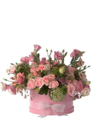 Arreglo de flores naturales con rosas en color rosado, lisianthus, greens y follaje en una caja redonda rosa.