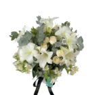Arreglo de flores naturales con lilis, rosas, astromelias y eucalipto en florero blanco de cerámica.