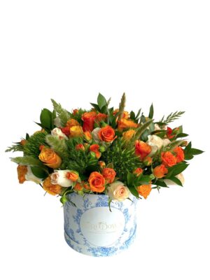 Arreglo de flores naturales con rosas naranjas y blancas en base blanca.